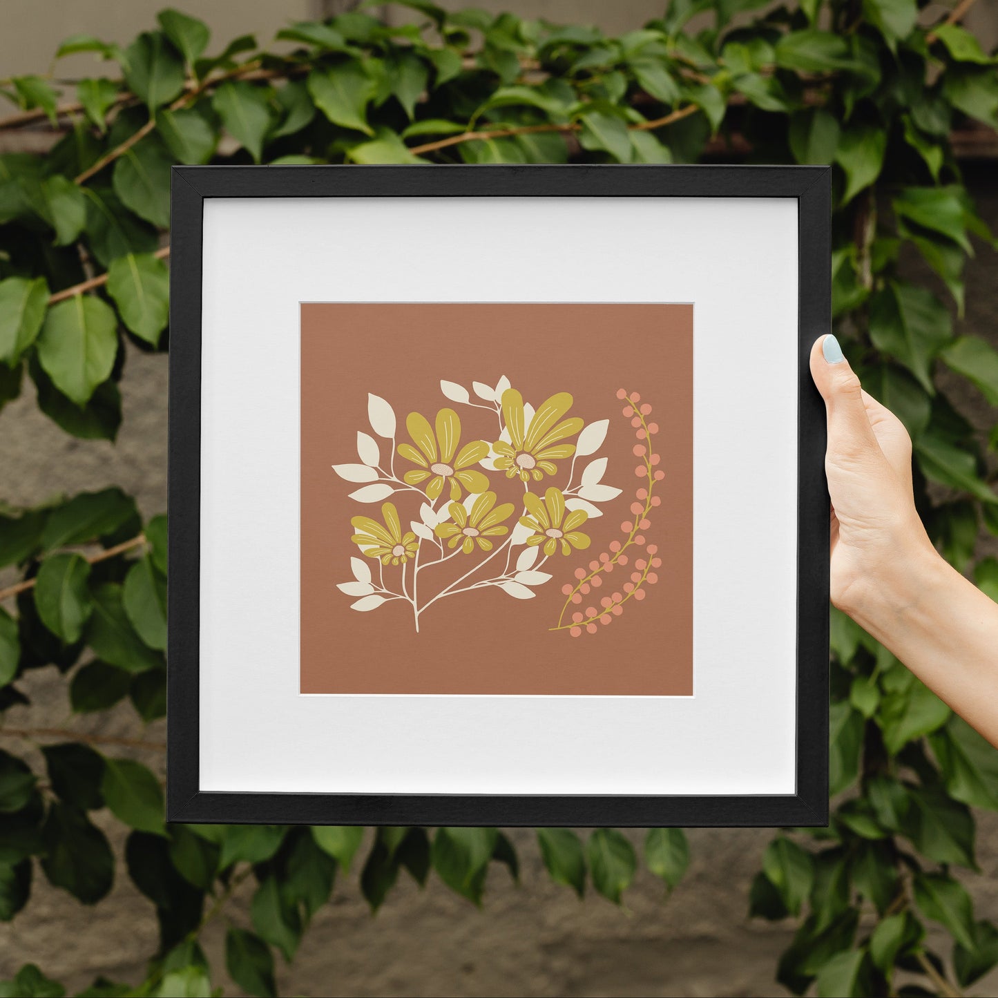 Framed artwork with a leaf design held in front of green foliage