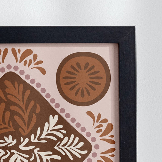 Decorative vase with dried plants next to a framed artwork on a white surface.