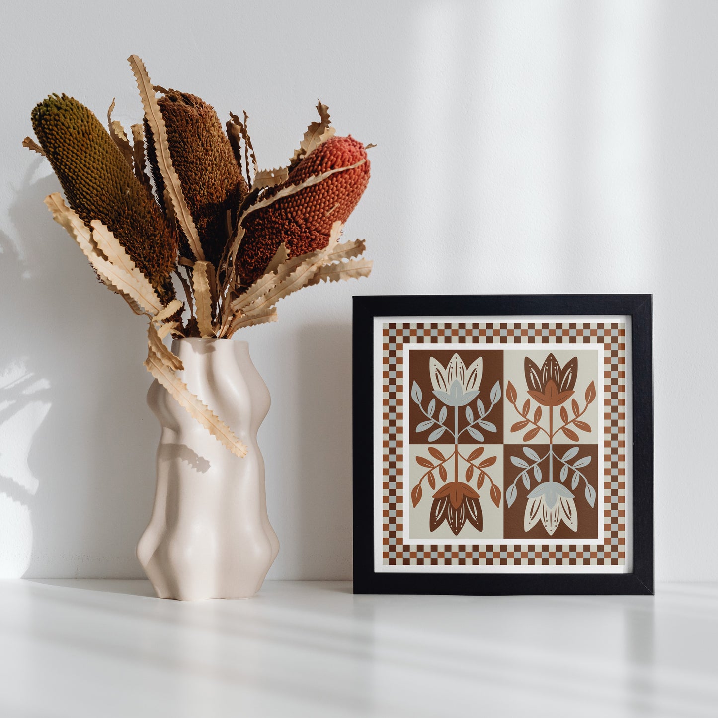 Framed 432 Design artwork with floral design next to a vase with dried plants on a white surface
